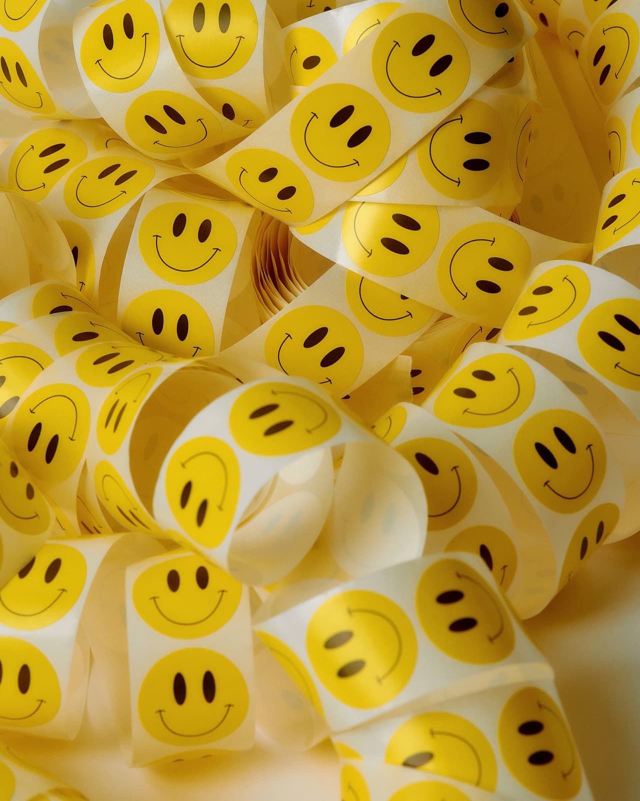 Strisce arricciate di adesivi tondi con faccine sorridenti, ammucchiate alla rinfusa una sull'altra