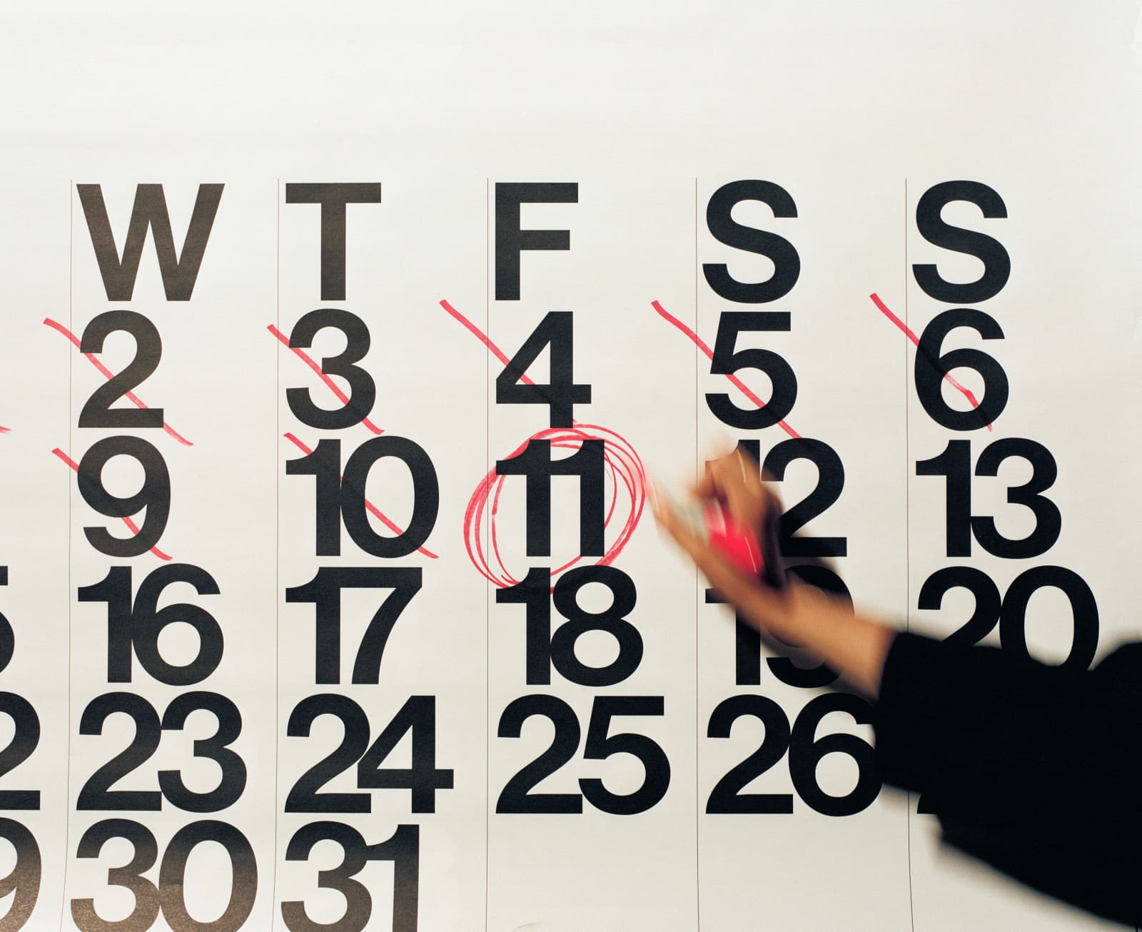 Mano con un pennarello rosso che cerchia l'11 su un grande calendario da parete, i giorni precedenti barrati